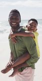 Vertical video of portrait of happy african american father with son at beach. family spending time together.