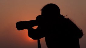A young photographer is taking pictures with a professional camera in the color of a golden summer sunset sky. - Powered by Shutterstock - Get 15% off with code: PIKWIZARD15