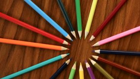 A lot of multicolored pencils revolve in a circle on a black wooden background. Concept office or school, knowledge day, the first of September. Video footage is spinning