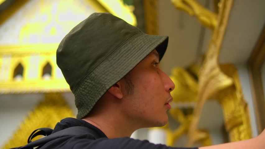 Profile of a young man in a bucket hat exploring ornate golden architecture, with a focus on cultural travel during the morning