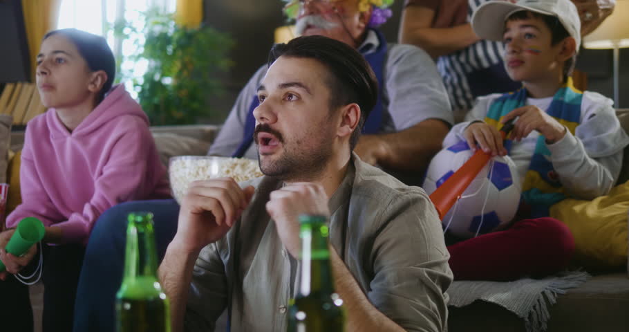 Soccer male fan watching sport match on a TV at home with his family, shows his displeasure after a missed goal Royalty-Free Stock Footage #3475383315