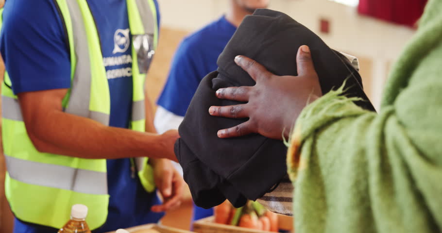 Volunteer, men and group with clothes to homeless for community service, poverty relief or donation in hall. NGO, collaboration and charity project with shelter, collection and giving back to support