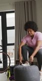 Vertical video of plus size biracial woman tying shoes at home. spending active time at home and body inclusivity.