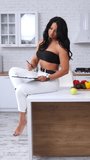 Beautiful fit lady sitting on the table and taking notes. Dark-haired woman thinking over nutrition plan. Healthy food concept. Vertical video