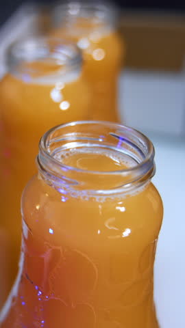 Food factory worker's hands in gloves put the caps on the bottles. Fresh apple juice in bottles being shut close up. Vertical video