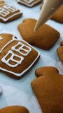 Handmade decoration of cookies at confectionery. Putting white glazing on a beautiful gingerbread houses. Close up. Vertical video