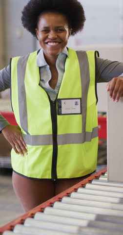 Vertical video of portrait of african american female worker with box in warehouse. global shipping and delivery business.