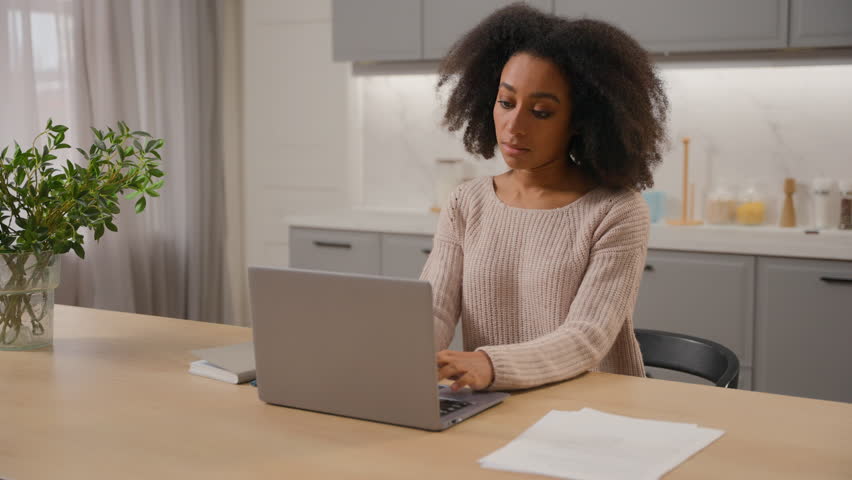African American woman freelancer online working from home with laptop in kitchen young ethnic girl female businesswoman writer pensive thinking create idea typing article on computer distant studying Royalty-Free Stock Footage #3475554343