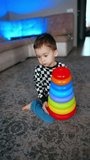 Young baby boy holding a colorful pyramid while sitting on the floor. Kid disassembles the toy and starts to build again. Vertical video.