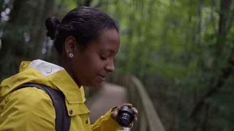 Young Latin woman wearing yellow rain jacket drinking of a sustainable metal water bottle taking a break on a hike on Nature. Active people hiking in the bush and forest. No plastic 스톡 비디오