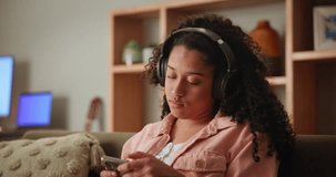 Girl, home and sofa on smartphone with headphone for music playlist and smile for entertainment. Female person, lounge and couch on internet for streaming service or social post and online video.