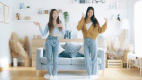 Two asian young woman recording trend dance video on smartphone in living room. Overjoyed teen girl dancing to favorite energetic music, having fun with joyful