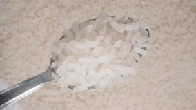 White rice grains on a metal spoon viewed from above against a background of rice, looped video as an advertising banner.