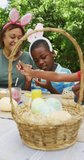 Vertical video of happy african american family painting eggs at easter. family spending time together at home.