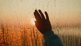 Sad person reaches hand to red sun behind wet window closeup. Palm silhouette on glass with raindrop pattern background. Negative emotions - Powered by Shutterstock - Get 15% off with code: PIKWIZARD15