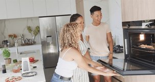 Young Asian man and biracial women share a high-five in a modern kitchen. Laughter fills the home as they enjoy a casual gathering with friends, slow motion.