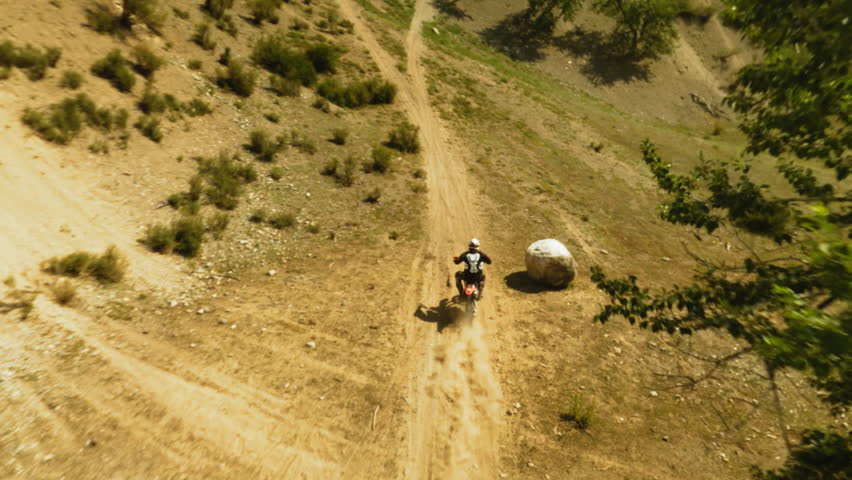 Motorbiker rides vehicle along ground road fpv drone. Extreme sportsman on motorcycle enjoys trip across hilly valley. Racing competition offroad