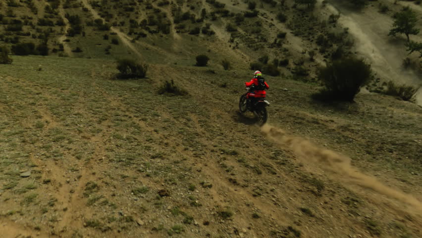 Person in red rides motorbike along bushy hills fpv. Fearless racer in helmet drives vehicle to mountain peak at motocross racing. Extreme sport at highland