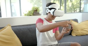 A young man wearing virtual reality headset playing game in living room. He holding controllers, laughing, enjoying immersive experience on couch, unaltered, slow motion