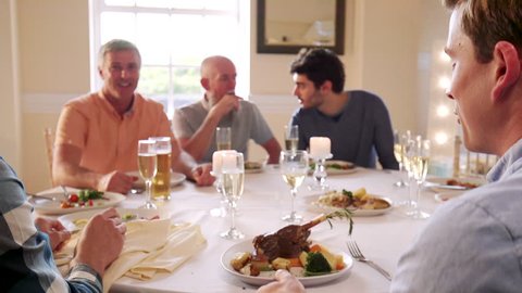 Men are eating at a dinner party. One man passes his plate for someone to put a piece of food on it. 