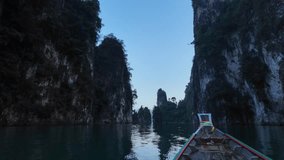 Point of view clip showing traditional wooden bow of boat moving through calm waterway in Thailand National park at sunset, a beautiful honeymoon destination