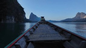 Timelapse clip showing front of wooden boat moving over calm lake in Thai National park, with steep rocky mountains and native rainforest