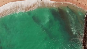 Video shooting from a drone of a sandy beach by the ocean with vacationing tourists. Aerial view of people during the summer holidays on seashore with azure water. Travel and summer holiday concept