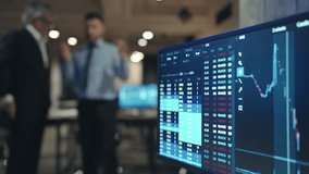 Camera view of computer display with financial data or crypto graphs. Man showing his fingers on display. Trading online. Stock market. Two men talking with each other in background. Business concept. - Powered by Shutterstock - Get 15% off with code: PIKWIZARD15