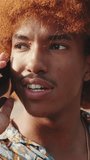Vertical video, Close-up of young guy talking on phone, sitting outside. Young man has joyful conversation and listens attentively