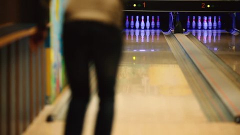 In the game club for bowling, the player throws a bowling ball that knocks down skittles. The focus on the pins, the player is blurred.