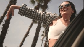 Excited woman enjoys the palm trees of seaside road. Girl leans out of the window of a rental car on a coastal highway on a sunny day. Hair in wind. A tropical vacation on the beach of exotic islands - Powered by Shutterstock - Get 15% off with code: PIKWIZARD15