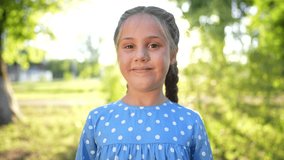 the little girl smiles. concept of happy childhood and loving family. girl schoolgirl looks at the camera and smiles widely, lifestyle face close-up, park and sun glare in the background - Powered by Shutterstock - Get 15% off with code: PIKWIZARD15