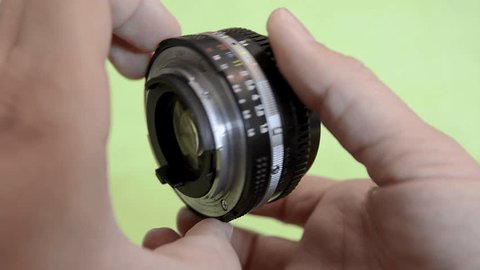 Short shot of a man's hands showing how the iris of a photography and video lens opens and closes on a green chroma key backgroundの動画素材