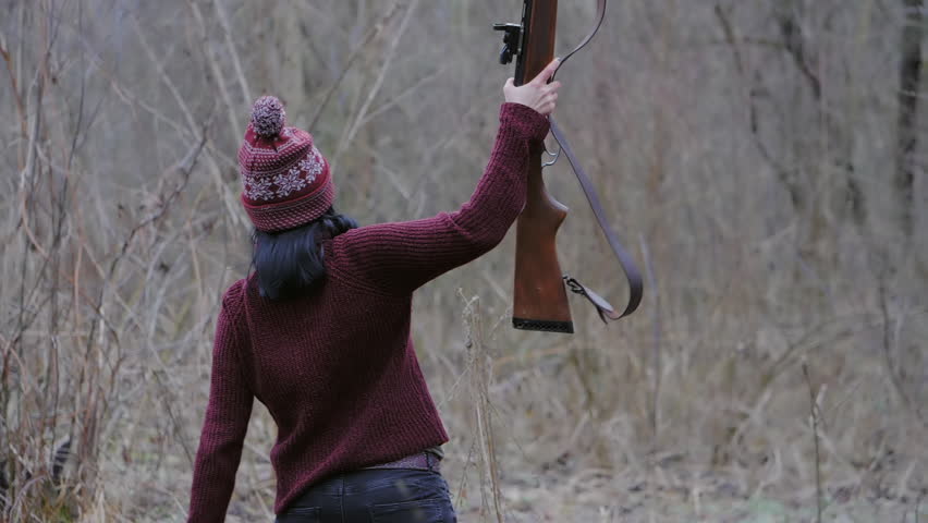Hunter woman in burgundy warm clothes with gun. Territorial defense. Girl hunting in the forest and rejoices her victory by raising rifle up after firing. Ukraine. Slow motion.