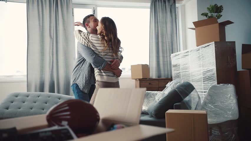 Nice Caucasian couple in love hugging and turning. Young people moving to new apartment. There are unpacked things, new sofa in living room. | Shutterstock HD Video #34760770