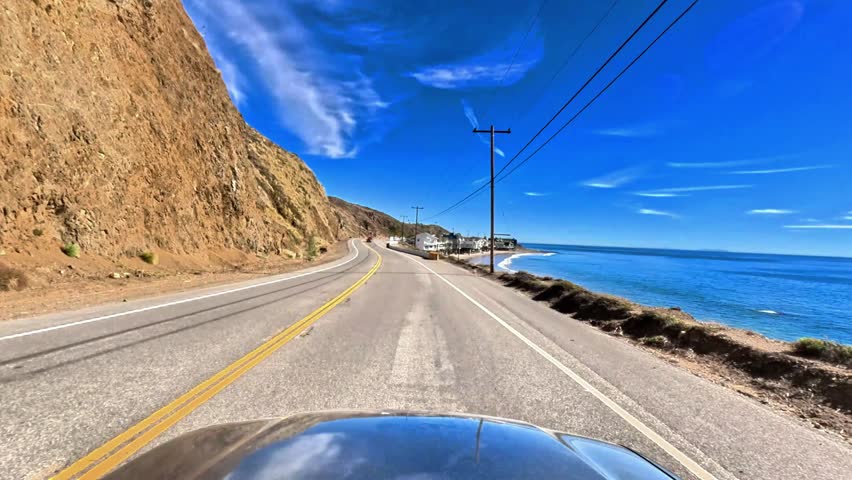 Relaxing point of view drive down the pacific coast highway in Malibu, California, USA.  Blue skies with wispy clouds and calms beaches.  The ideal American road trip of freedom.