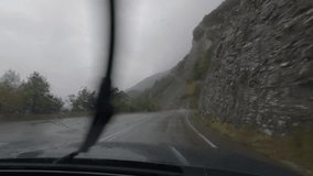 First person view, FPV, from dashcam of car driving in the Pyrenees mountains on the border of Spain, France, Andorra in a storm. Road trip video in POV from inside vehicle, with rain and dark skies