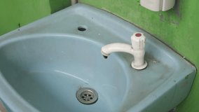 An Asian man in a red shirt is attempting to turn on the tap, but no water flows out. Conceptual image of water supply issues or malfunctioning plumbing. Shot against a neutral background.
