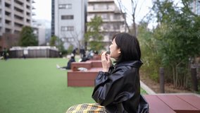 Slow motion video of a young Japanese woman in her 20s eating churros in a park around Gotanda Station, Shinagawa-ku, Tokyo in winter