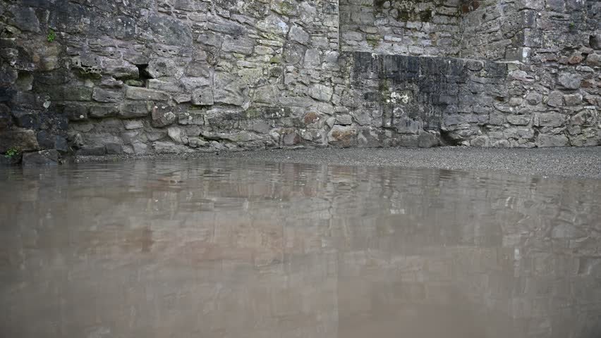 A rippling puddle in castle ruins before being disturbed by someone in blue jeans and black boots
