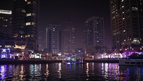 Dubai, United Arab Emirates. December 23, 2017. Night city, panoramic view -  "Dubai Marina". People walk and relax on the quay. Boat floats on the channel.