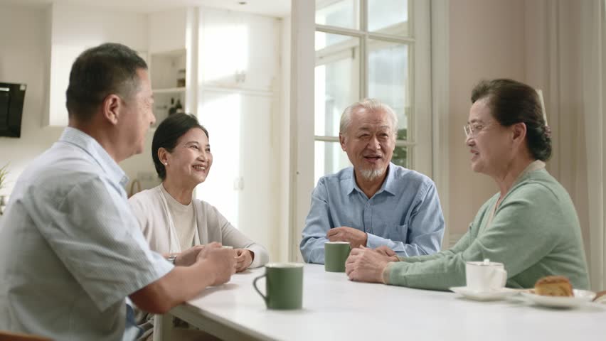 group of happy senior asian people two couples sitting at table at home enjoying a pleasant conversation