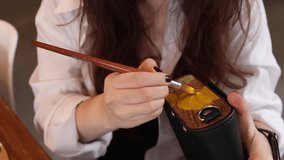 Woman hand painting with acrylic colors on wooden and leather bag. Female hand holding brush close up on horizontal video. Artist working process