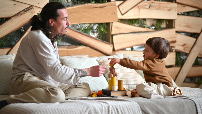 Father playing with his son with colourful, ecological wooden toys on the bed