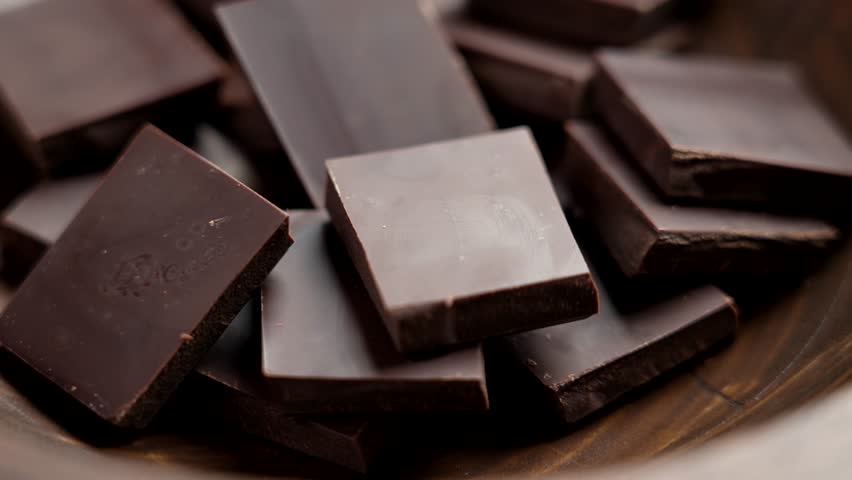 Dark bitter chocolate pieces in wooden brown rustic bowl. Food pleasure concept. Rotation. Macro shot