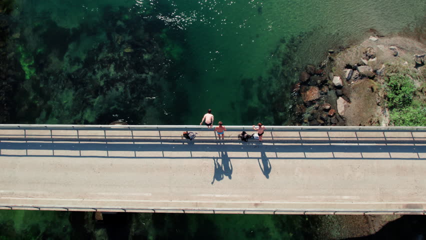 Drone shot of group of friends have summer fun on warm and sunny day in the mountains, jump into river from bridge, adventure and adrenaline, youthful fun
