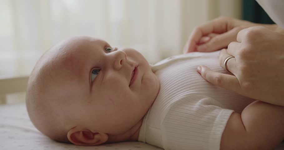 Closeup of mother talking tenderly with infant baby, hold her little hands and kiss at nursery room. newborn smiling with her mom. Loving mom taking care about her newborn baby. Motherhood concept.