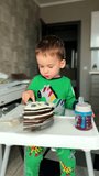 A quarter of chocolate cake with blueberries is on the table in front of the baby boy. Cute kid takes a piece and smiles. Vertical video.