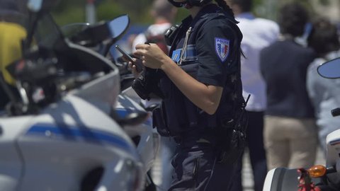 Female police officer standing next to motorbike, checking mobile phone on duty