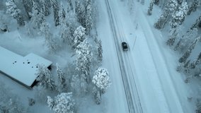 A drone captures a black van driving on a snowy road near the Arctic Circle in Luosto, Finland, offering a breathtaking aerial view.